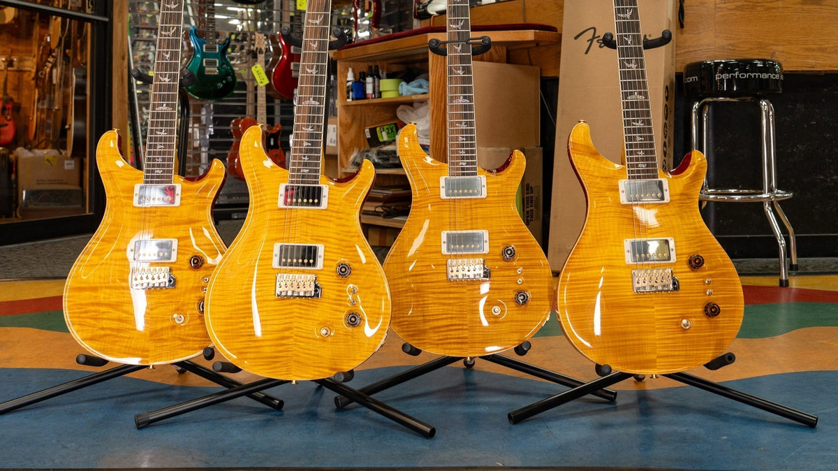 Four PRS Wood Library McCarty Tremolo guitars in Vintage Yellow on stands at Chuck Levin's