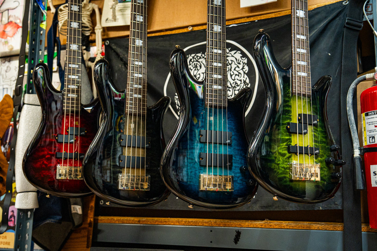 Four Spector ICON NS Neck Through basses on the wall at Chuck Levin's in Purple Cherry, Black Stain, Black and Blue, and Haunted Moss